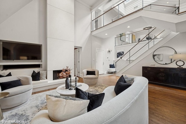 living room with stairs, a fireplace with raised hearth, a high ceiling, and wood finished floors