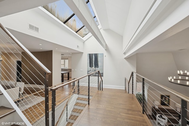 hallway with baseboards, visible vents, wood finished floors, an upstairs landing, and high vaulted ceiling