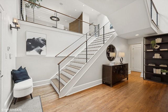 stairway featuring wood finished floors, a towering ceiling, and baseboards