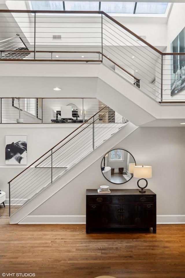 stairs with a high ceiling, wood finished floors, visible vents, and baseboards