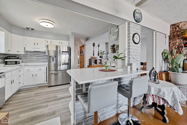 kitchen with light countertops, appliances with stainless steel finishes, white cabinets, and a kitchen breakfast bar