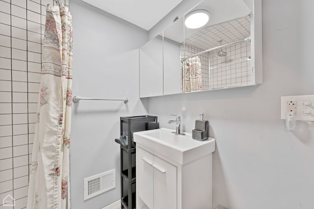 bathroom featuring visible vents, tiled shower, and vanity