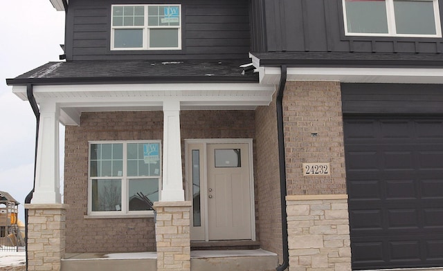 property entrance with board and batten siding, brick siding, and roof with shingles