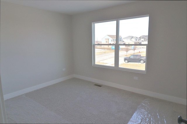 carpeted empty room featuring visible vents, a healthy amount of sunlight, and baseboards