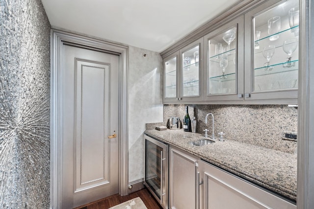 bar featuring sink, wine cooler, decorative backsplash, light stone counters, and dark wood-type flooring