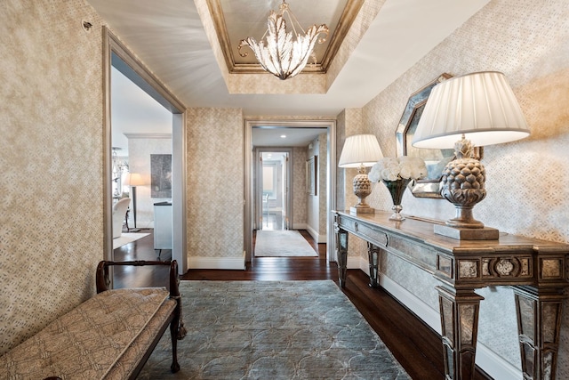 hallway featuring a raised ceiling, ornamental molding, dark hardwood / wood-style floors, and a chandelier