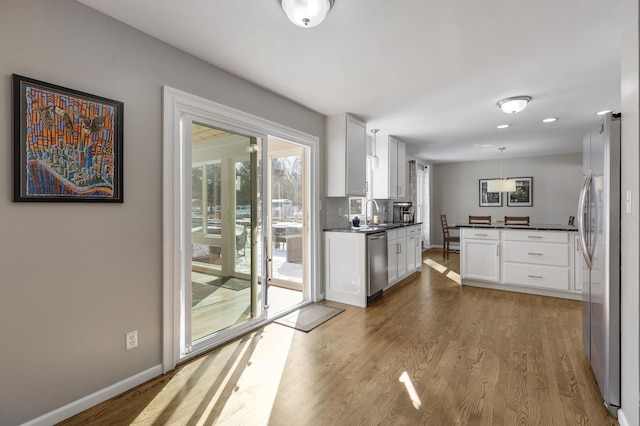 kitchen featuring stainless steel appliances, wood finished floors, white cabinetry, hanging light fixtures, and dark countertops