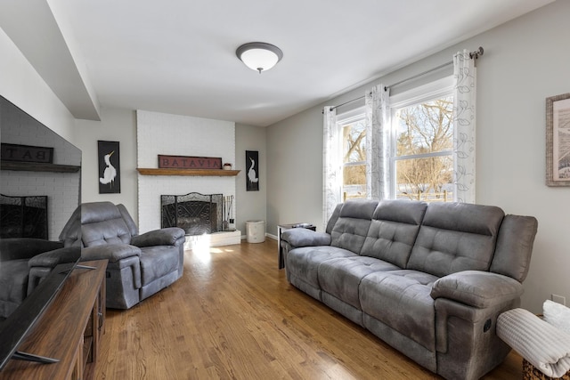 living area featuring light wood-type flooring, a brick fireplace, and baseboards