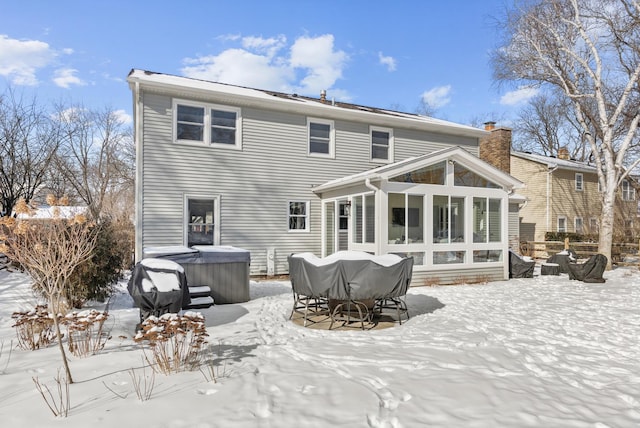 snow covered house with a sunroom, a hot tub, and a chimney