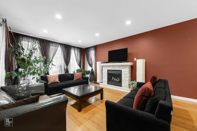 living area with recessed lighting, baseboards, a stone fireplace, and light wood finished floors