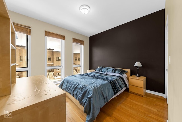 bedroom with light wood-type flooring, an accent wall, and baseboards