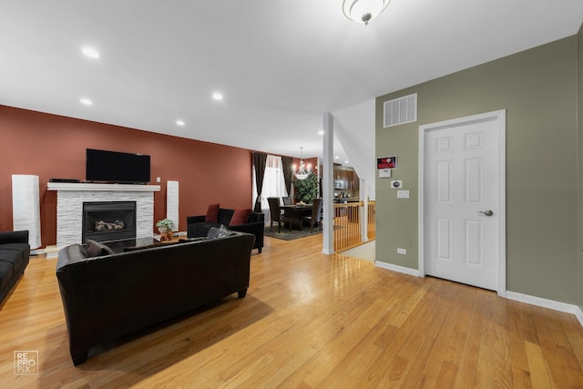 living area featuring a chandelier, light wood-style flooring, a fireplace, visible vents, and baseboards