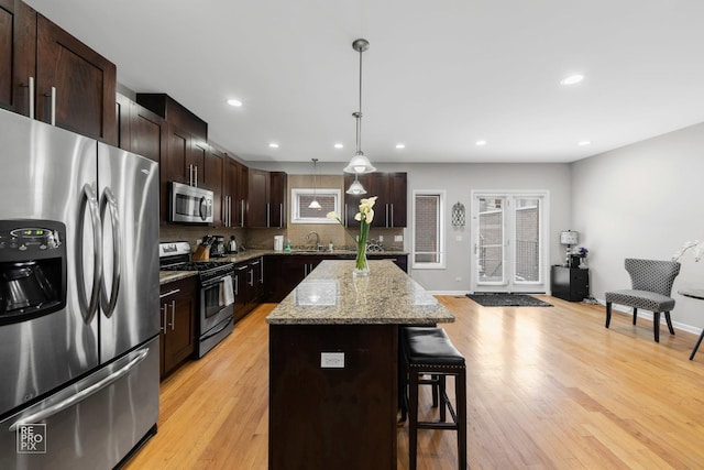 kitchen featuring a kitchen breakfast bar, a center island, hanging light fixtures, light stone countertops, and stainless steel appliances