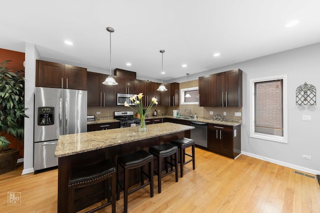 kitchen with stainless steel appliances, decorative light fixtures, a kitchen island, and a kitchen bar