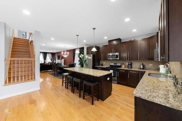 kitchen featuring a breakfast bar area, light wood-style flooring, a sink, a kitchen island, and appliances with stainless steel finishes