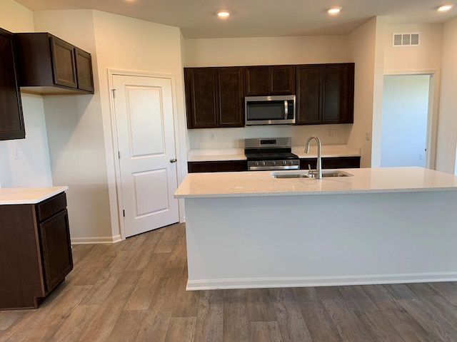 kitchen featuring appliances with stainless steel finishes, sink, a center island with sink, and light hardwood / wood-style flooring