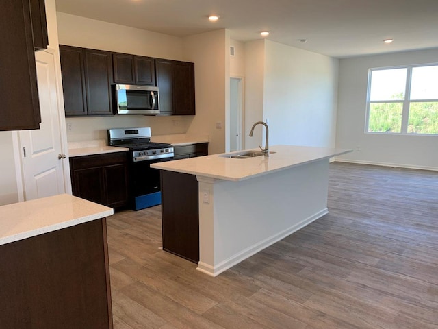 kitchen featuring sink, a kitchen island with sink, dark brown cabinetry, stainless steel appliances, and light wood-type flooring