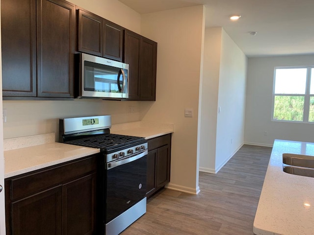 kitchen with light stone counters, stainless steel appliances, light hardwood / wood-style floors, and dark brown cabinets