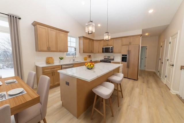 kitchen with sink, light stone counters, decorative light fixtures, a center island, and stainless steel appliances