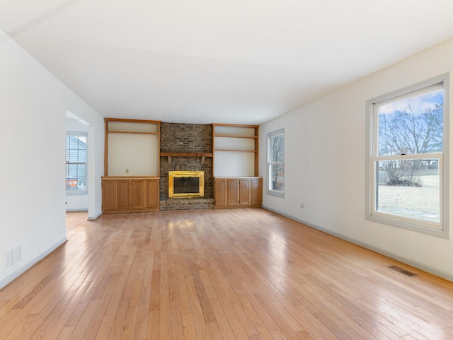 unfurnished living room featuring a brick fireplace, a wealth of natural light, and light hardwood / wood-style floors