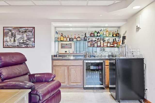 bar with light tile patterned floors, sink, a paneled ceiling, beverage cooler, and black refrigerator