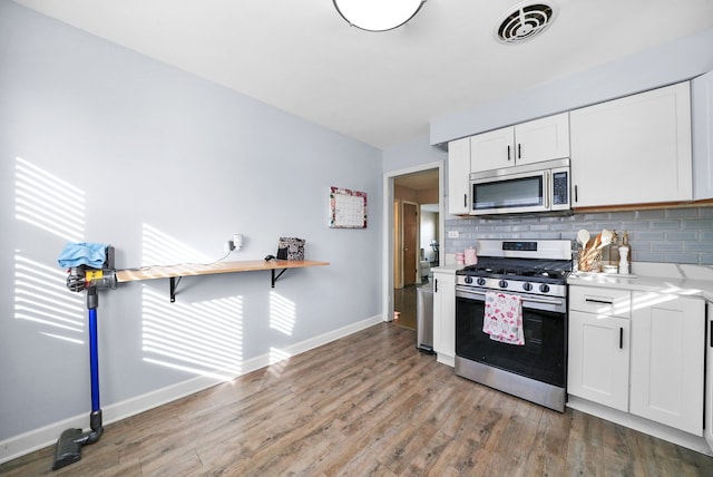 kitchen with wood-type flooring, appliances with stainless steel finishes, white cabinets, and backsplash