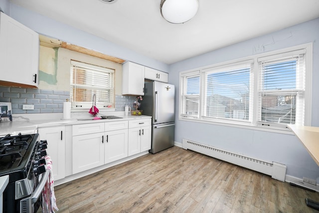 kitchen with sink, white cabinetry, stainless steel appliances, light hardwood / wood-style floors, and a baseboard radiator