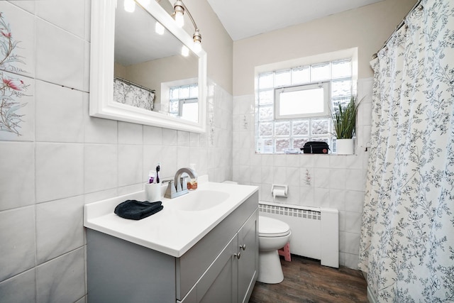 bathroom featuring radiator heating unit, tile walls, hardwood / wood-style flooring, vanity, and toilet