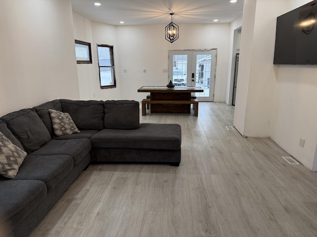 living room featuring an inviting chandelier, light hardwood / wood-style flooring, and french doors