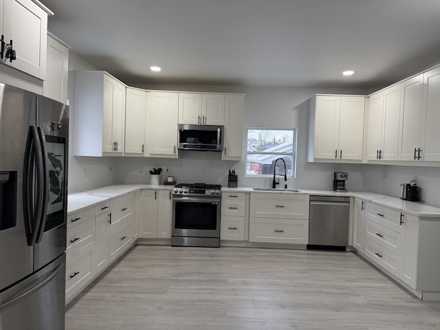 kitchen with white cabinetry, appliances with stainless steel finishes, light hardwood / wood-style floors, and sink