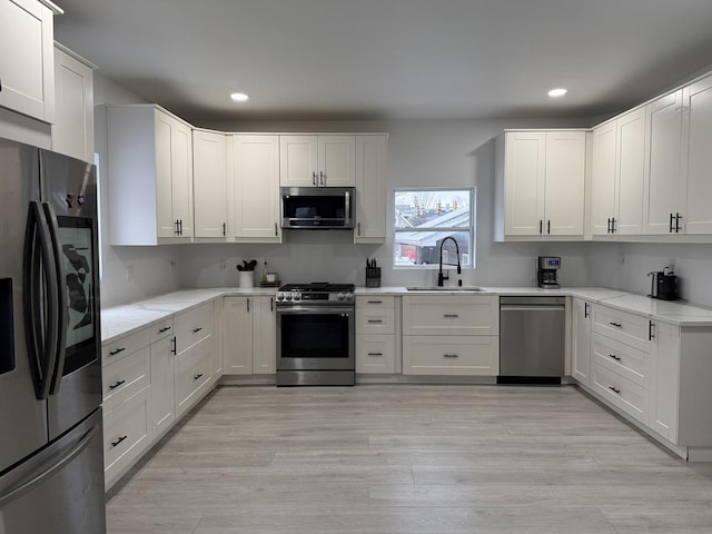 kitchen with white cabinetry, sink, light wood-type flooring, and appliances with stainless steel finishes