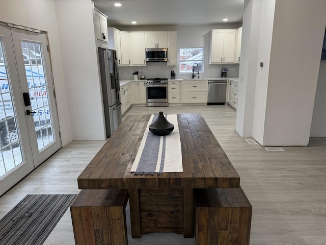 kitchen with white cabinetry, sink, stainless steel appliances, light wood-type flooring, and french doors