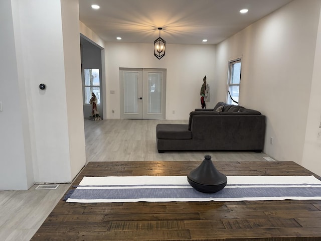 living room featuring a healthy amount of sunlight, a chandelier, light hardwood / wood-style floors, and french doors