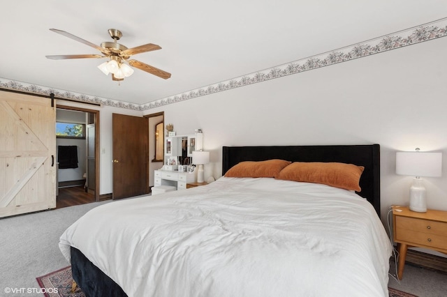 bedroom with ceiling fan, a barn door, and dark carpet