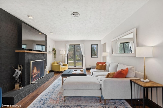 living room featuring a brick fireplace, dark wood-type flooring, and a textured ceiling