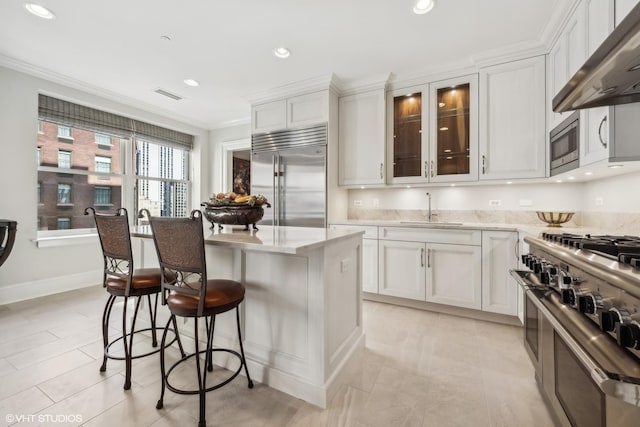 kitchen with white cabinetry, sink, a center island, built in appliances, and light stone countertops