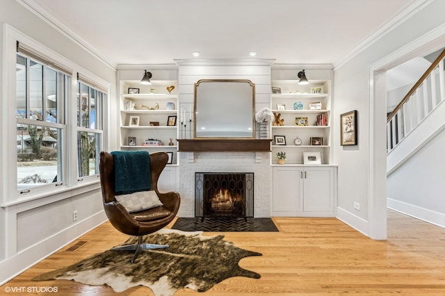 sitting room featuring a brick fireplace, crown molding, light hardwood / wood-style flooring, and built in shelves