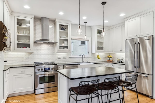 kitchen featuring high quality appliances, white cabinetry, a kitchen breakfast bar, a center island, and wall chimney exhaust hood