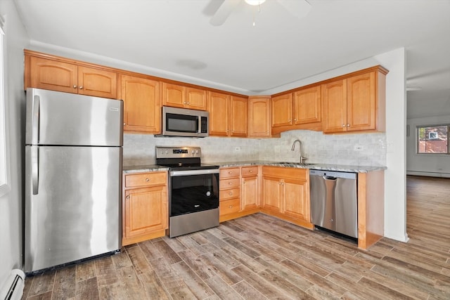 kitchen featuring sink, baseboard heating, backsplash, stainless steel appliances, and light hardwood / wood-style floors