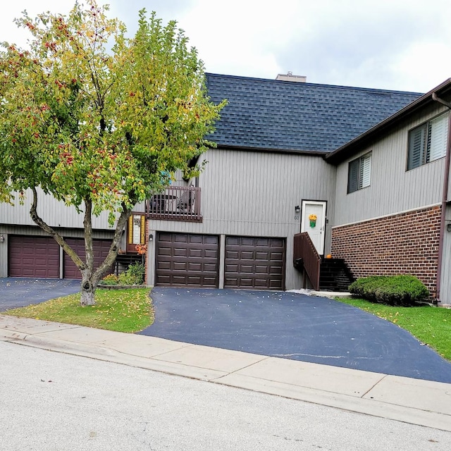 view of front facade with roof with shingles, driveway, a garage, and brick siding