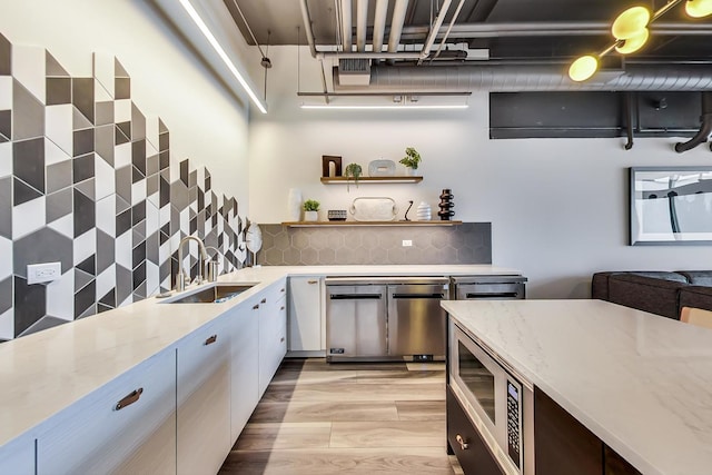 kitchen featuring a sink, white cabinetry, decorative backsplash, open shelves, and stainless steel microwave