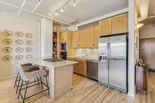 kitchen with a breakfast bar area, light countertops, light wood-style flooring, appliances with stainless steel finishes, and a sink