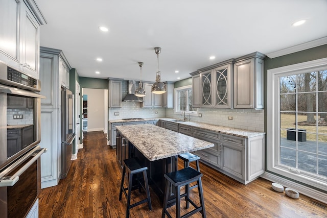 kitchen featuring appliances with stainless steel finishes, gray cabinetry, a center island, and wall chimney range hood