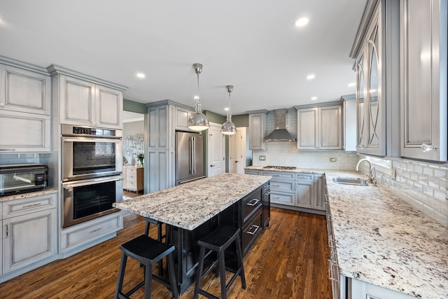 kitchen with gray cabinets, appliances with stainless steel finishes, a kitchen island, and wall chimney range hood