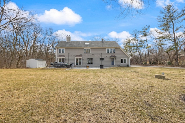 rear view of property with an outbuilding, a patio, a yard, a chimney, and a storage unit