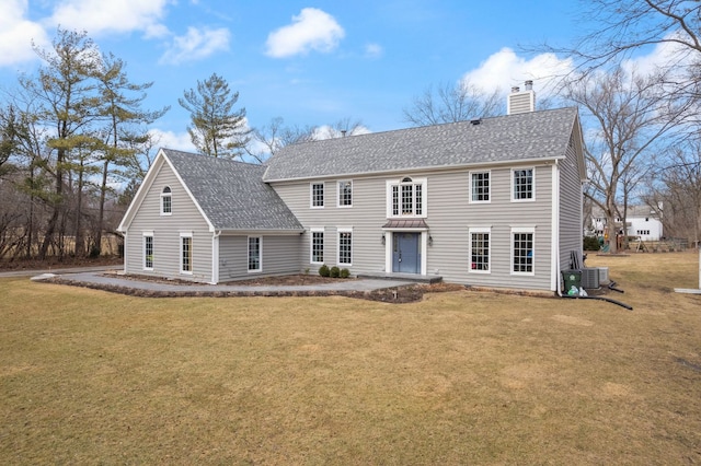 colonial inspired home with central air condition unit, a front lawn, a chimney, and roof with shingles