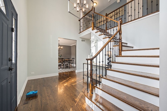 entrance foyer with baseboards, a chandelier, stairs, a towering ceiling, and wood finished floors