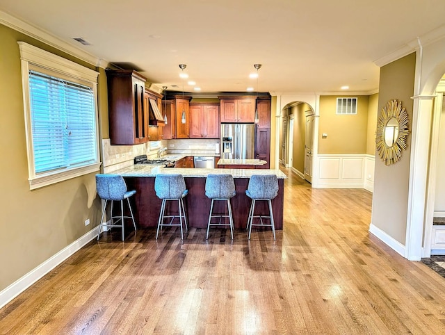 kitchen with appliances with stainless steel finishes, a kitchen bar, hanging light fixtures, kitchen peninsula, and crown molding