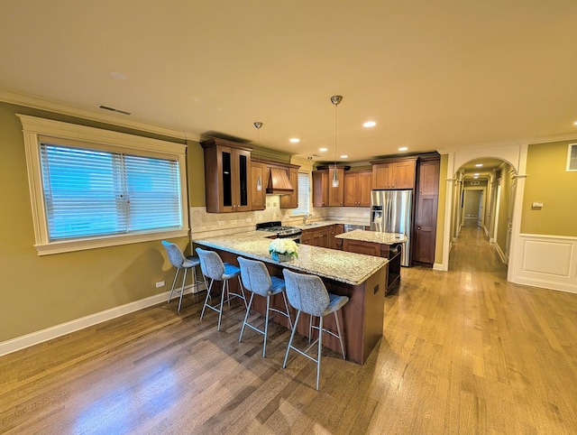 kitchen with decorative light fixtures, a kitchen breakfast bar, kitchen peninsula, stainless steel appliances, and light hardwood / wood-style flooring