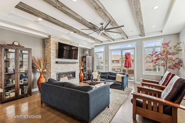 living room featuring beam ceiling, a stone fireplace, baseboards, and wood finished floors